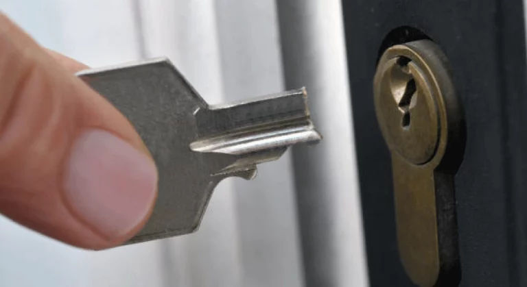 Image d'une main tenant une clé cassée devant un trou de serrure sur une porte.